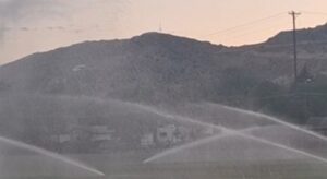 Water sprinkles arcing over a field with mountain silhouettes at dusk